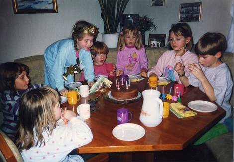 Geburtstagsfeier mit Torte - sieben Kinder sitzen um einen Tisch, das Geburtstagskind bläst gerade die Kerzen aus.
