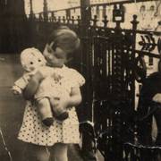 Mädchen mit Puppe auf einem Balkon vor großstädtischem Hintergrund
